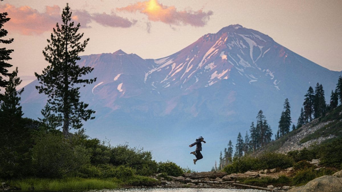 A person leaps joyfully in front of a scenic mountain during a beautiful evening. via Pexels