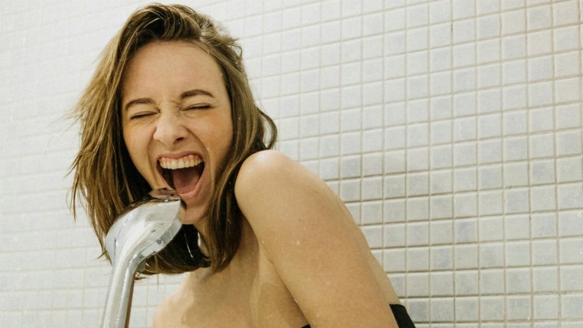 A joyful woman sings with a shower head in a bathroom, showcasing her playful spirit. via Pexels