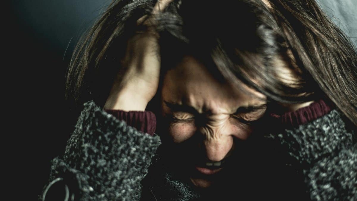 Close-up of a woman in distress with eyes closed and hands in hair, expressing anxiety. via Pexels