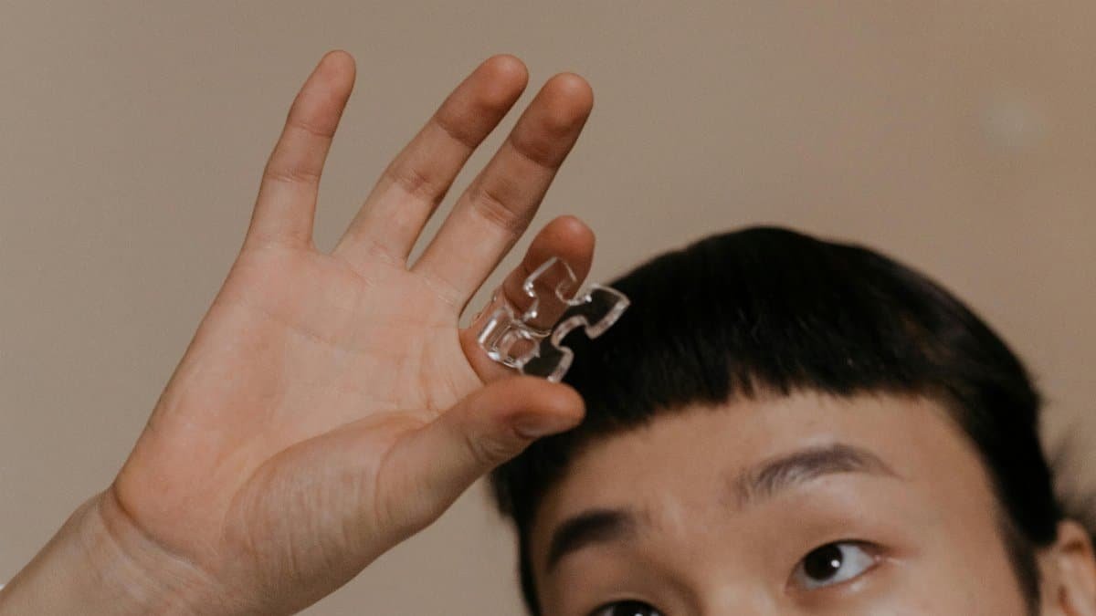 Person holding a transparent puzzle piece, focusing on the hand and expression. via Pexels