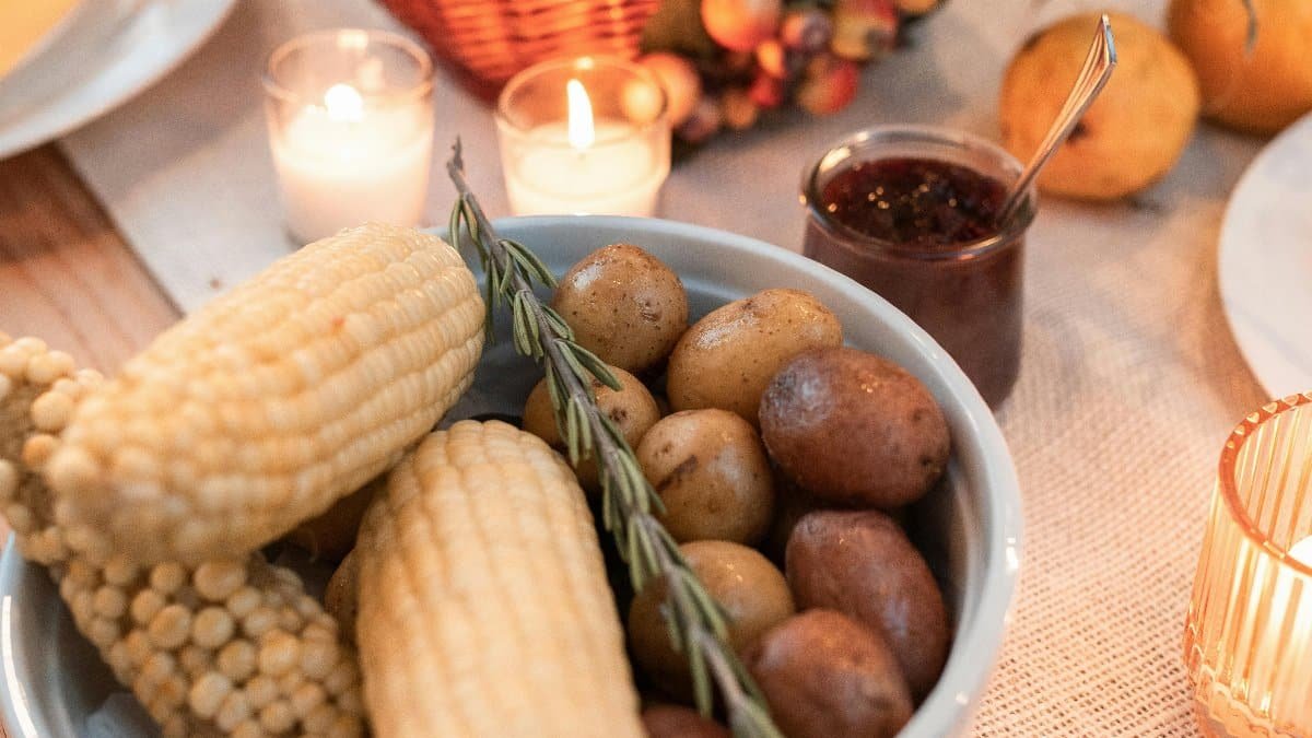 Warm autumn table setting with corn, potatoes, and harvest decor, perfect for Thanksgiving. via Pexels