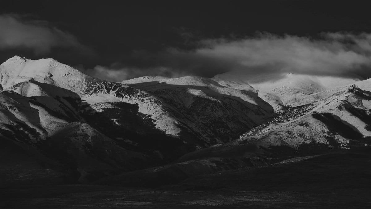 A striking black and white photograph of snow-covered mountain peaks under a cloudy sky. via Pexels