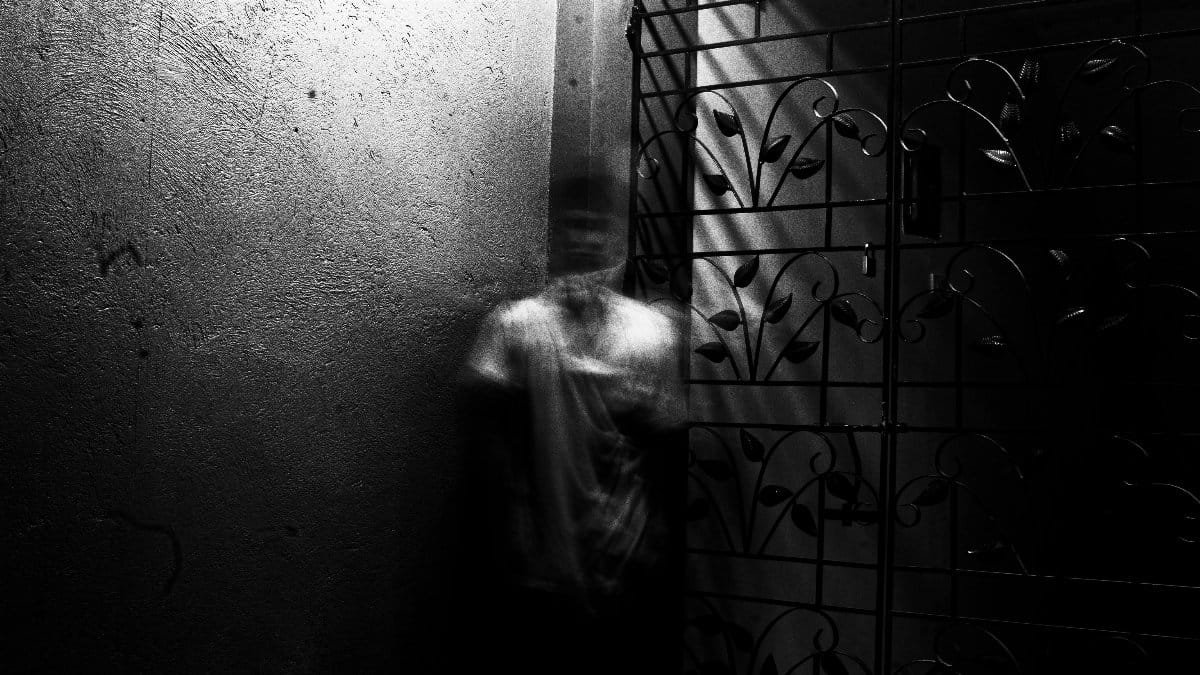 Grayscale photo of a blurred figure in an eerie indoor setting with metalwork. via Pexels