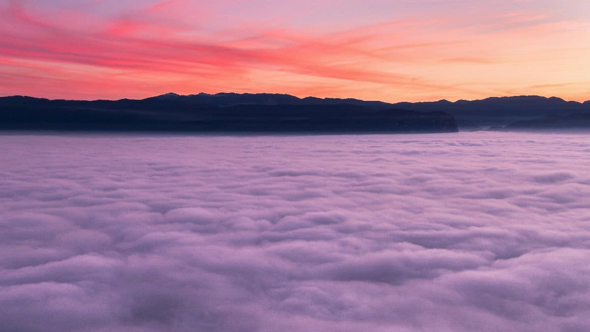 A breathtaking view of the sunset casting vibrant colors over a fog-covered valley and distant mountains. via Pexels