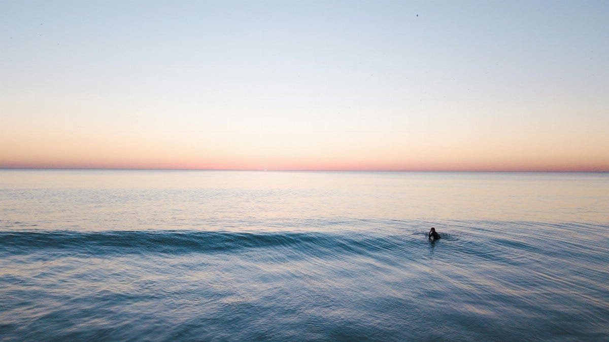 A lone surfer catches a wave at dawn, with a serene and pastel sky. via Pexels