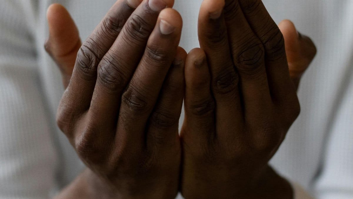 Selective focus of crop anonymous African American man wearing white turtleneck praying with open hands via Pexels