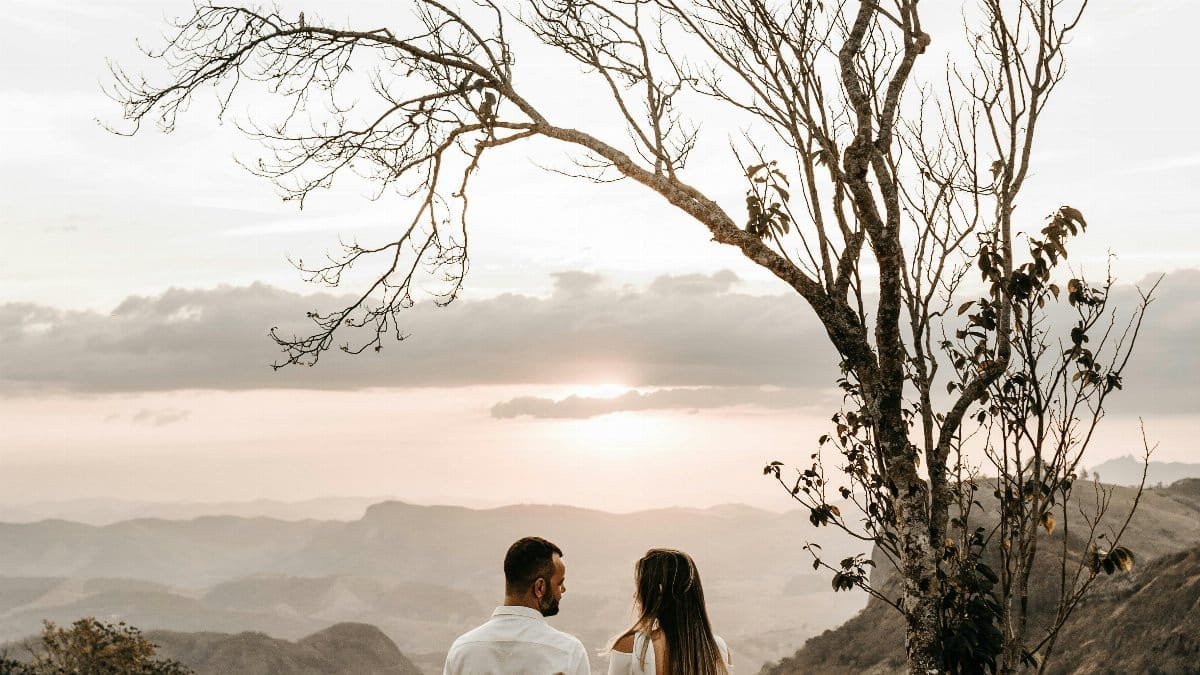 A romantic couple stands lovingly together at sunset with a breathtaking mountain view. via Pexels