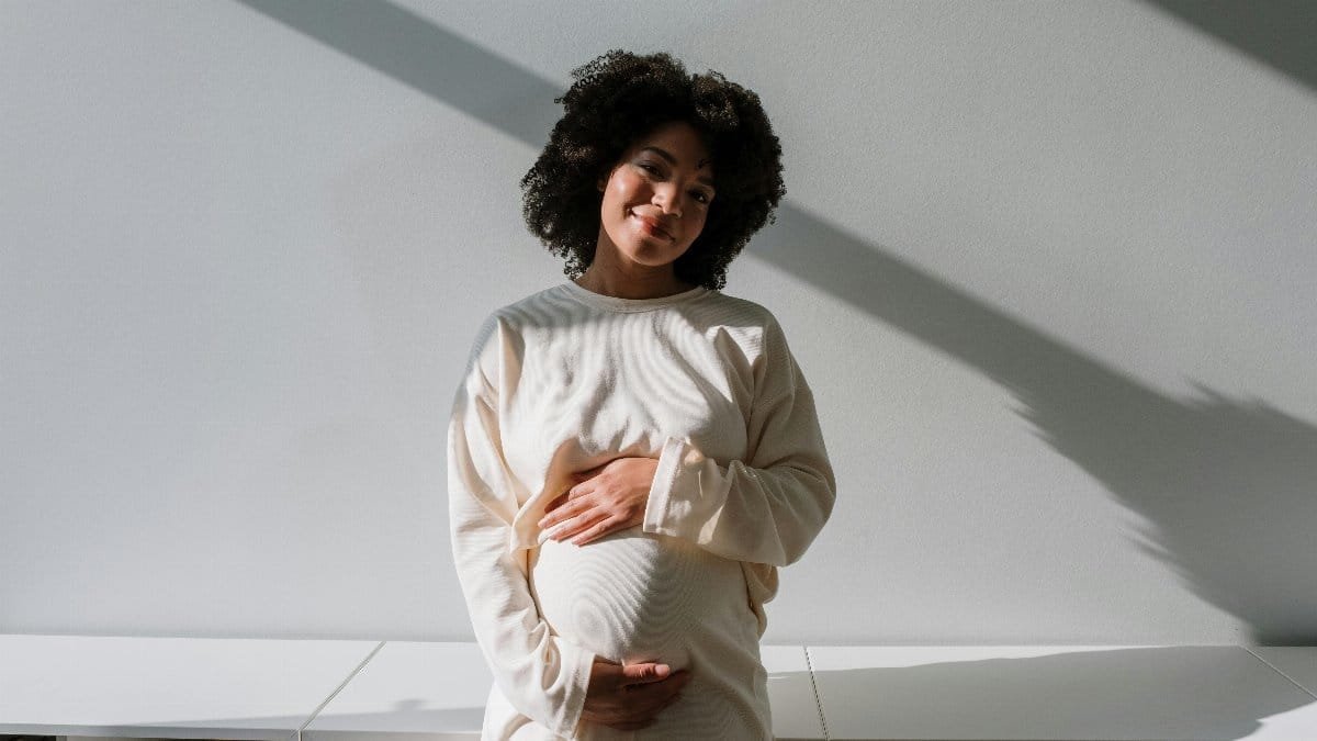 Beautiful pregnant woman with curly hair embracing maternity in a serene indoor setting. via Pexels