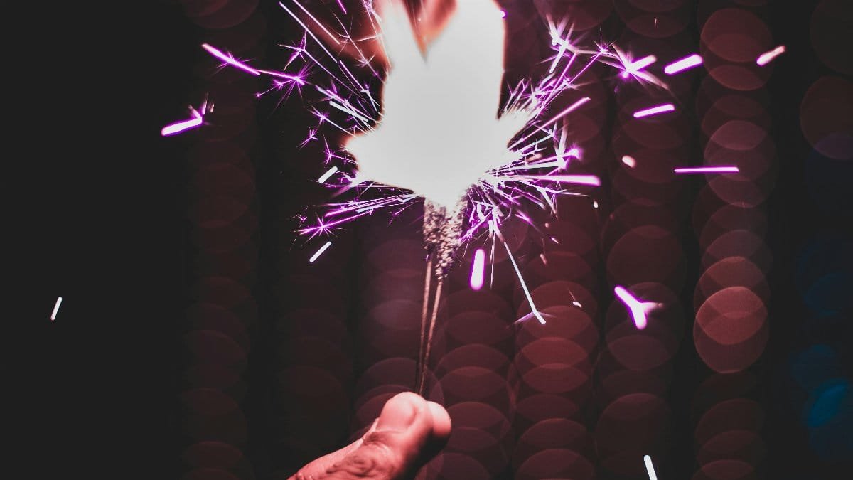 A close-up of a hand holding a sparkler with a vibrant bokeh background, creating a festive mood. via Pexels