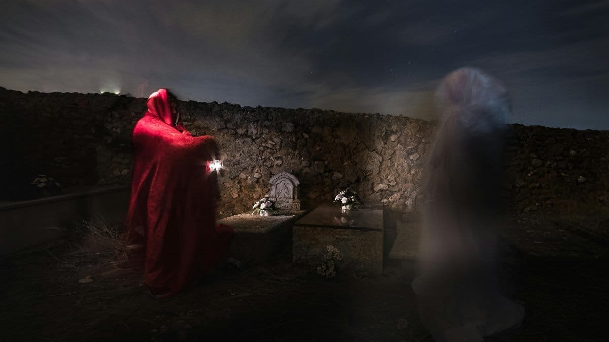 Night scene in a cemetery with a ghostly figure and a person in a red cloak, creating a mysterious atmosphere. via Pexels