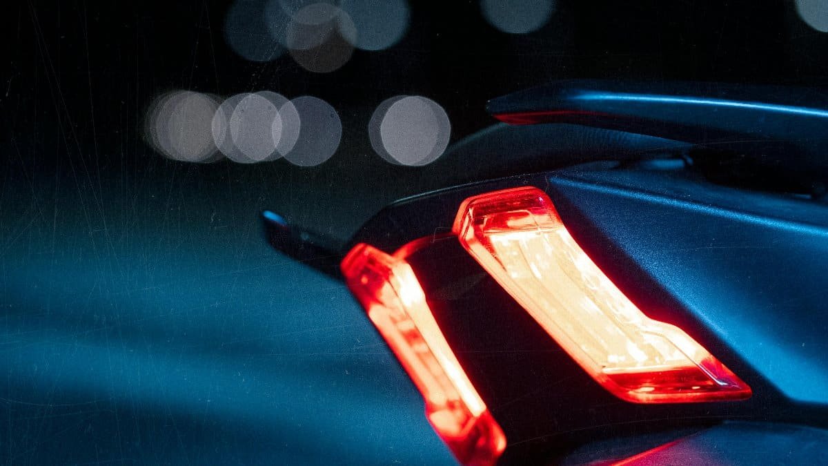 A detailed view of a motorcycle taillight glowing brightly against the dark night, showcasing vibrant bokeh. via Pexels