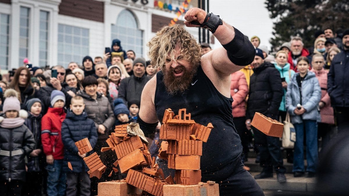 A strongman showcases strength by breaking bricks in front of a captivated crowd outdoors. via Pexels