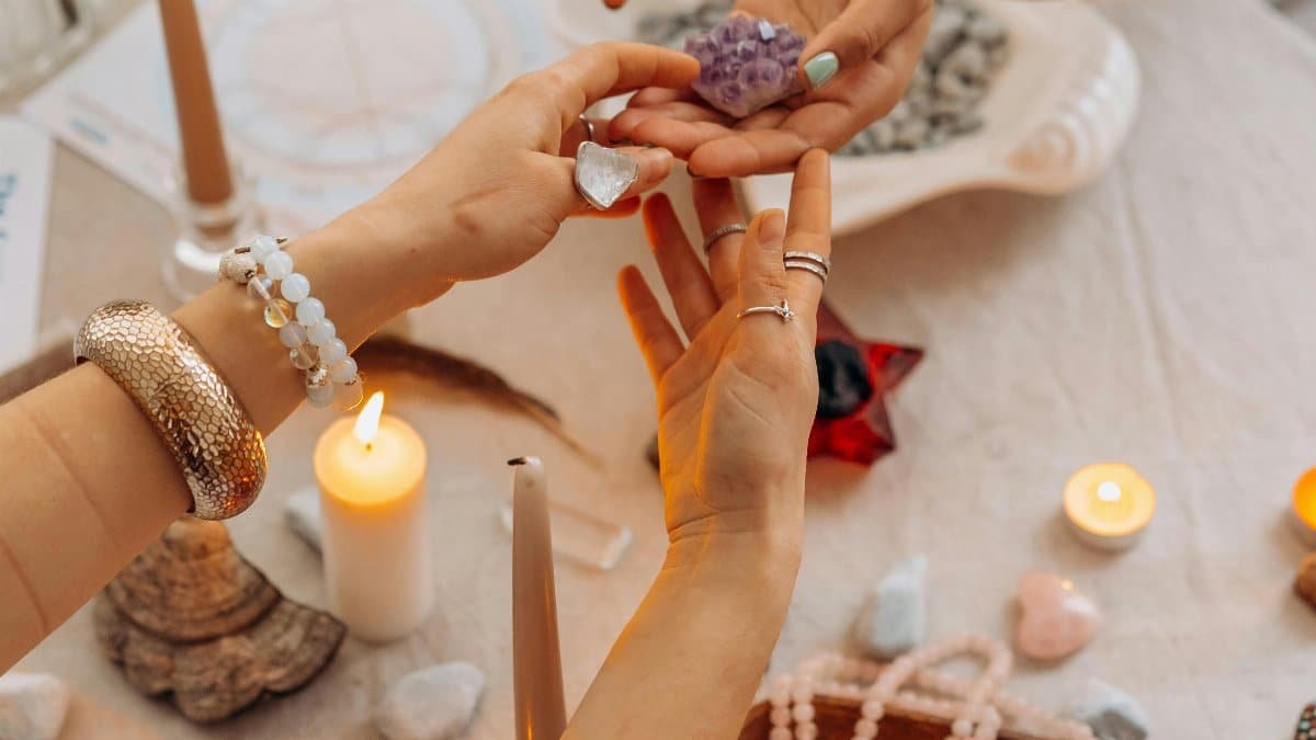 A serene indoor setting with hands exchanging healing crystals, surrounded by candles and spiritual items. via Pexels