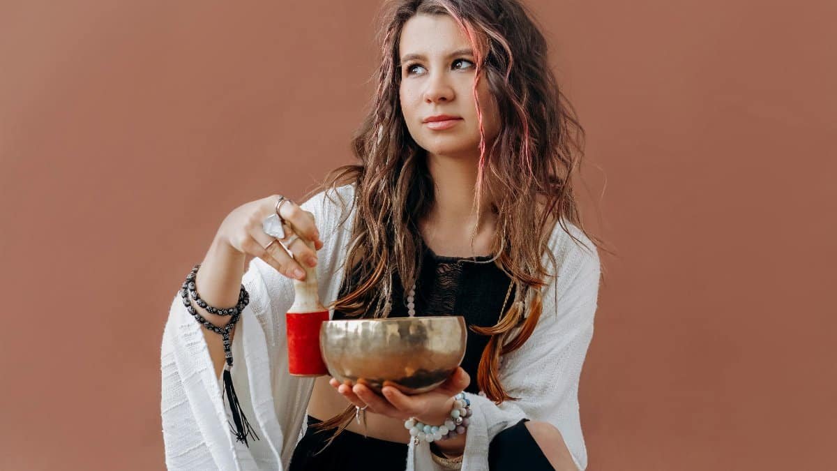 Young woman in black dress meditating with a singing bowl, embodying tranquility and focus. via Pexels