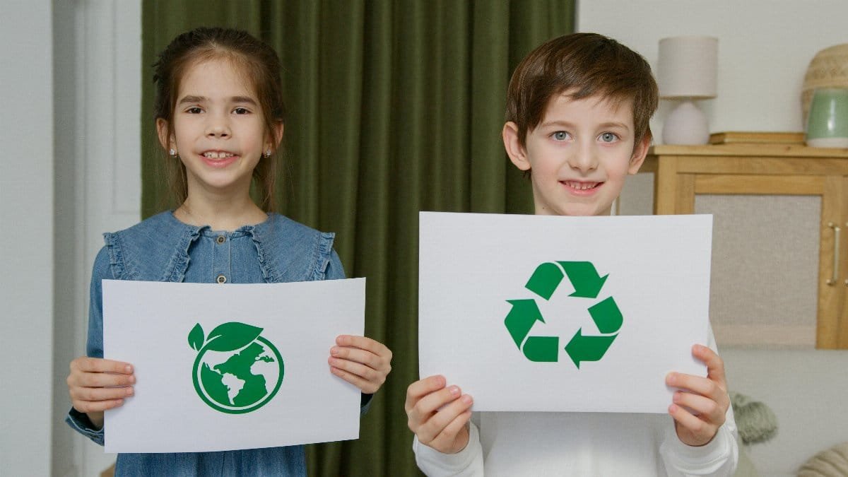 Two children holding eco-friendly signs indoors, promoting sustainability. via Pexels