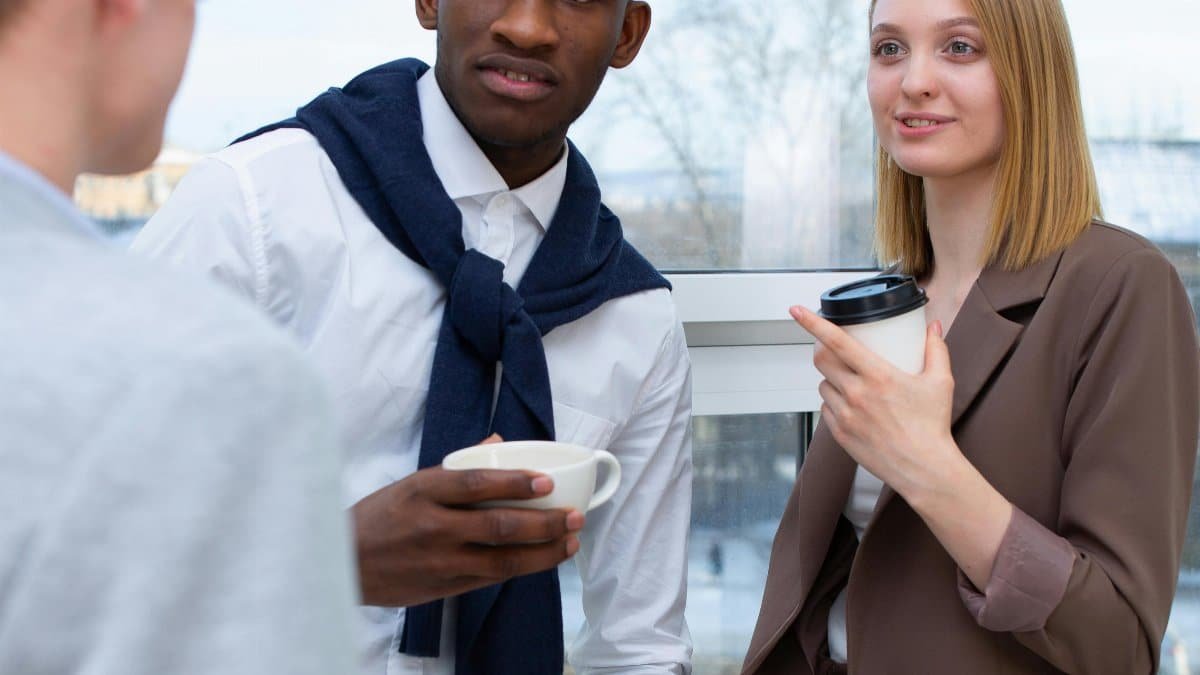 Diverse professionals sharing a coffee break at the office, enjoying conversation. via Pexels