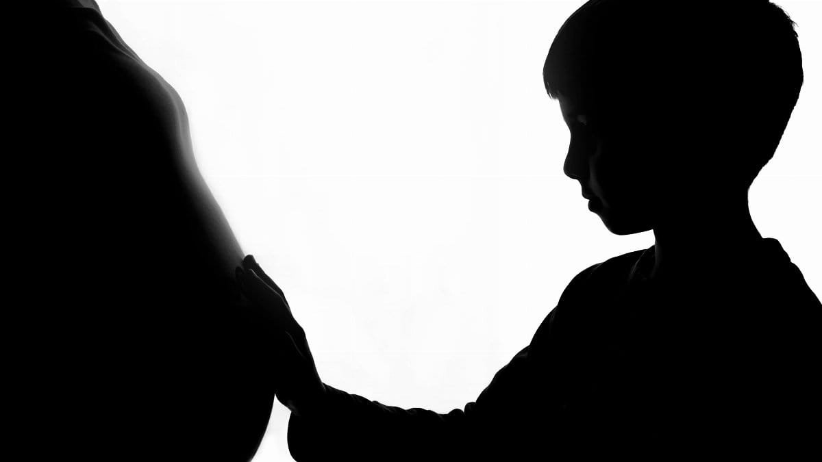 Silhouette of a boy gently touching a pregnant belly, creating a heartwarming connection. via Pexels