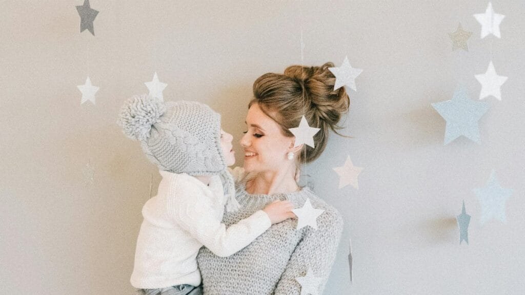 A loving mother embraces her child indoors with star decorations in the background. via Pexels