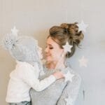 A loving mother embraces her child indoors with star decorations in the background. via Pexels