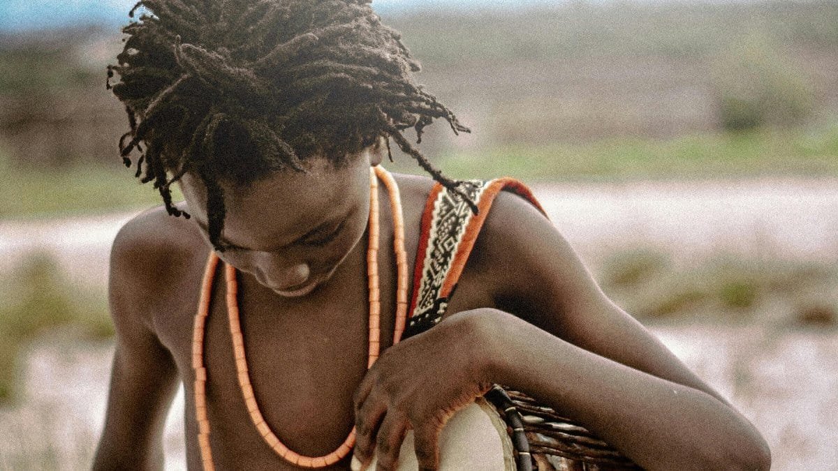 A young person playing a traditional African djembe drum outdoors. via Pexels