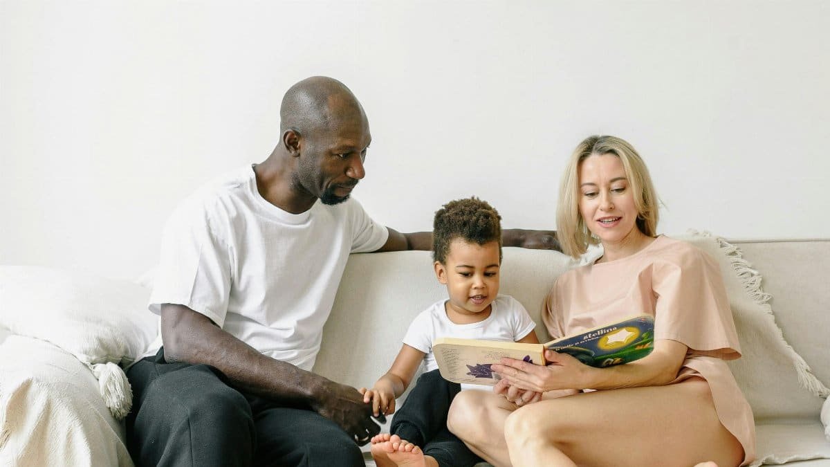 A diverse family enjoying quality reading time together indoors on a cozy couch. via Pexels