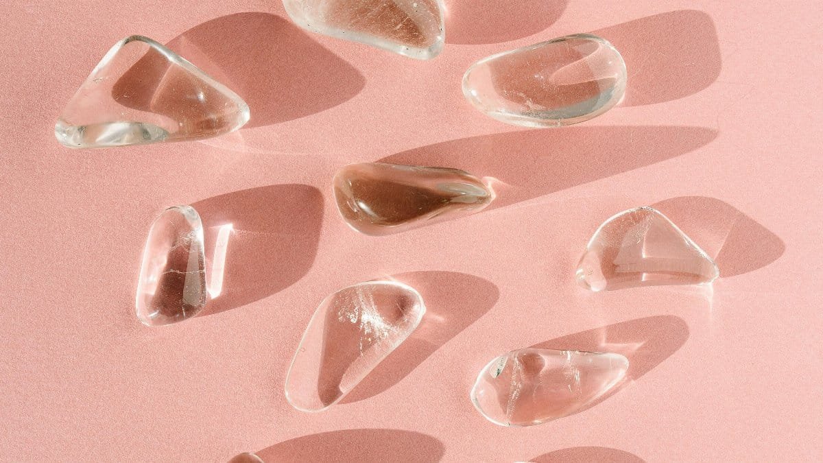 An artistic arrangement of clear quartz crystals casting shadows on a pink surface. via Pexels