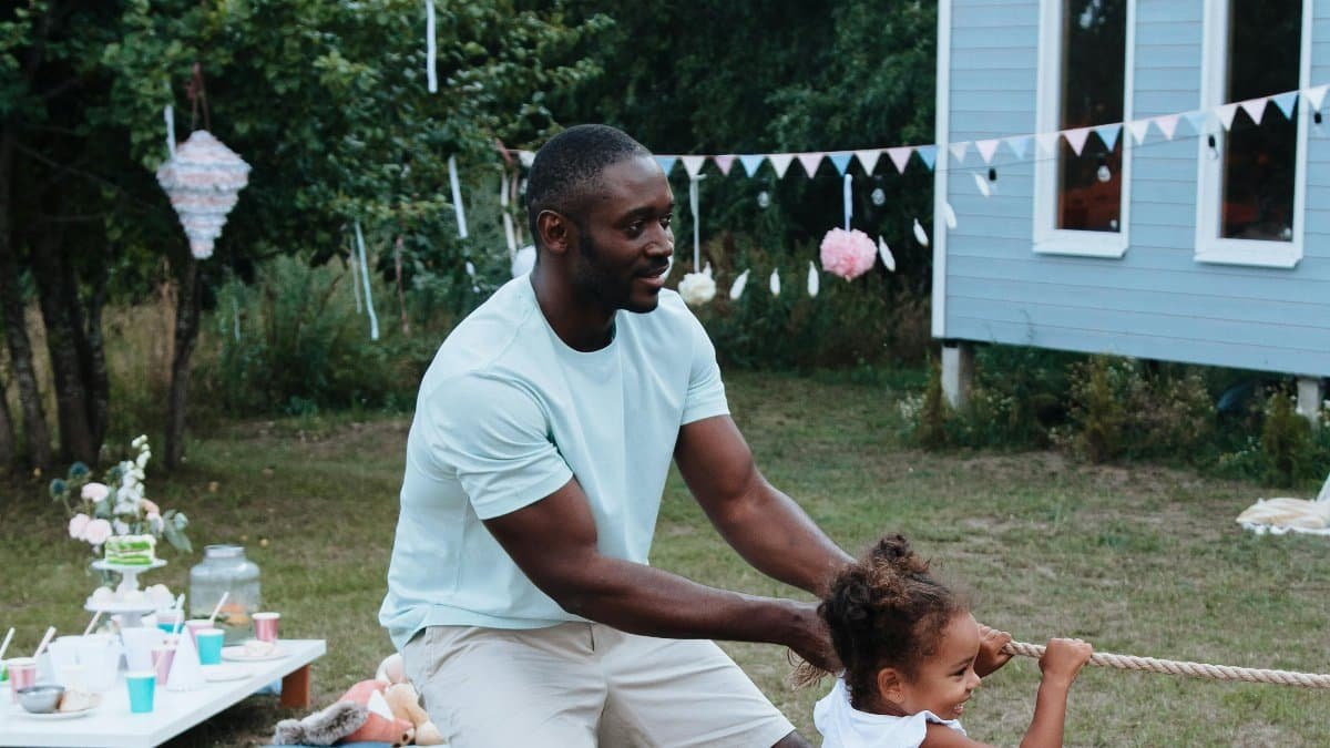 A joyful father-daughter tug-of-war game in a backyard setting. via Pexels