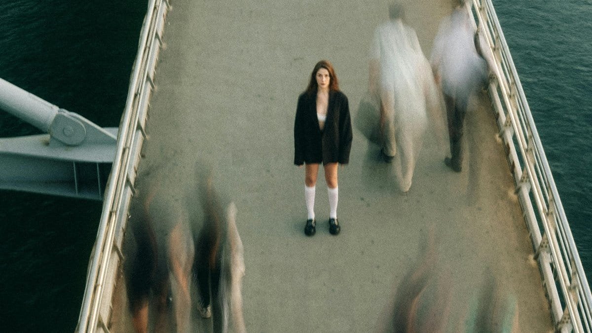 A woman stands still on a bustling footbridge, capturing a moment of solitude amidst motion. via Pexels