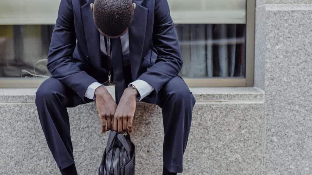 A businessman in a suit sits with his head down, expressing sadness and stress. via Pexels