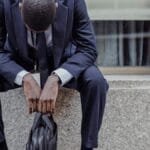 A businessman in a suit sits with his head down, expressing sadness and stress. via Pexels