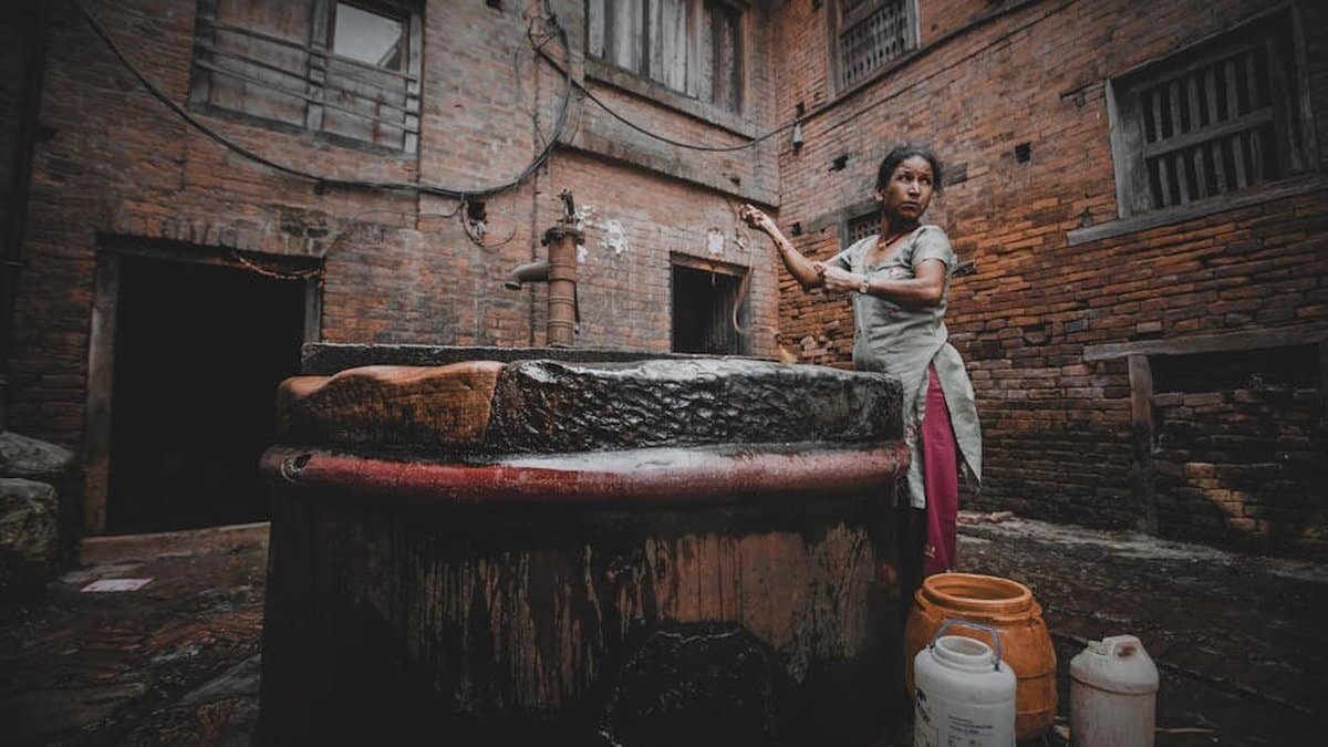 A woman fetching water from a traditional well in a historical town courtyard. via Pexels