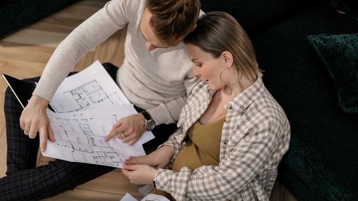 A couple sits on the floor reviewing house blueprints in their living room. via Pexels