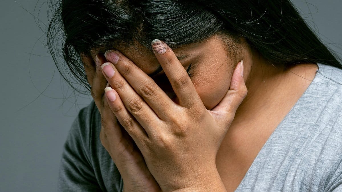 A woman hides her face in hands showing deep emotion and sadness in a studio setting. via Pexels