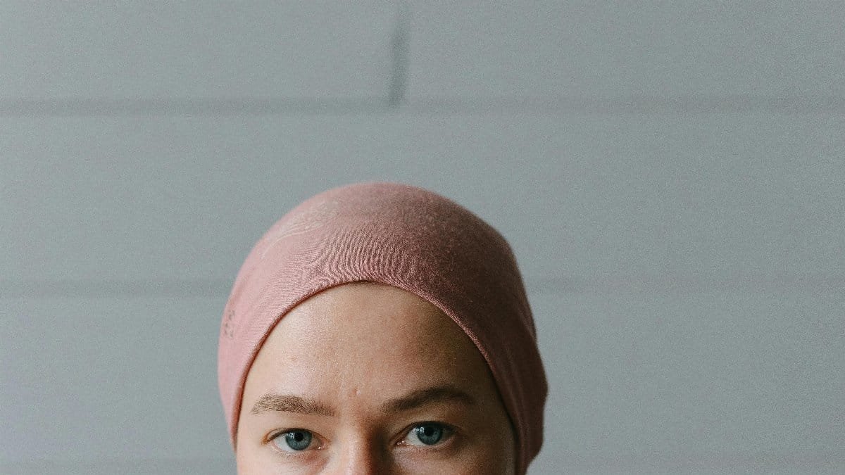 Close-up portrait of a woman wearing a pink headscarf and plaid shirt, conveying strength and resilience. via Pexels
