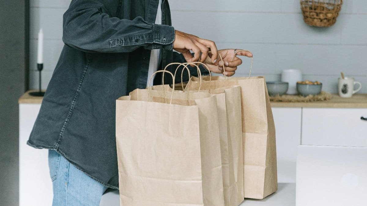 Young man organizing paper shopping bags indoors in a modern kitchen setting. via Pexels