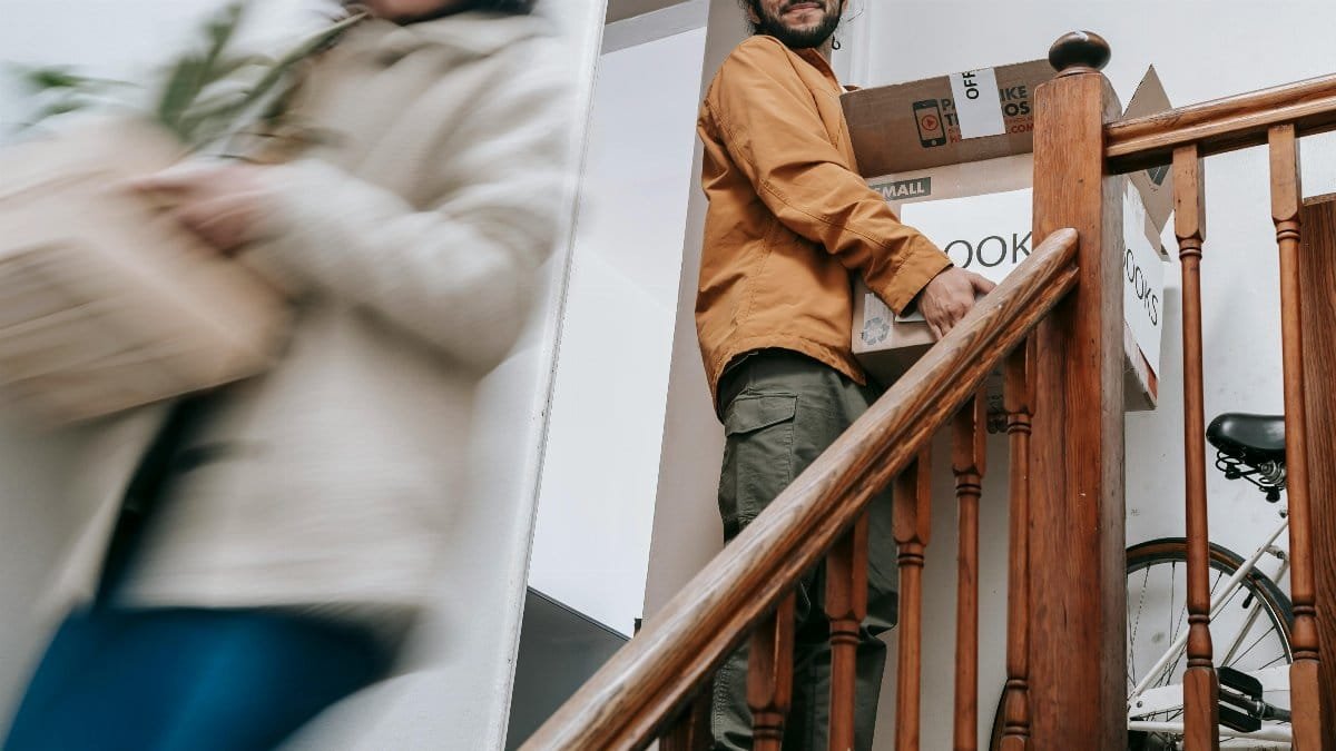 A joyful couple moving into their new apartment, carrying boxes and plants upstairs. via Pexels