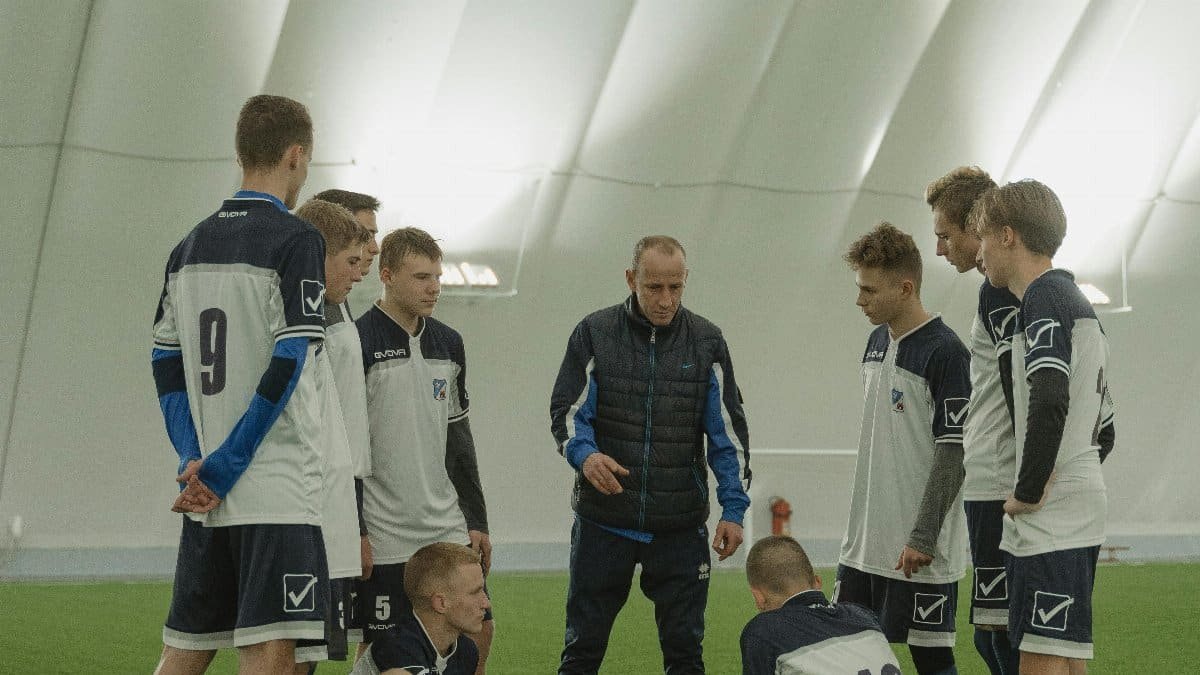 A coach giving a motivational talk to a youth soccer team inside an indoor stadium. via Pexels