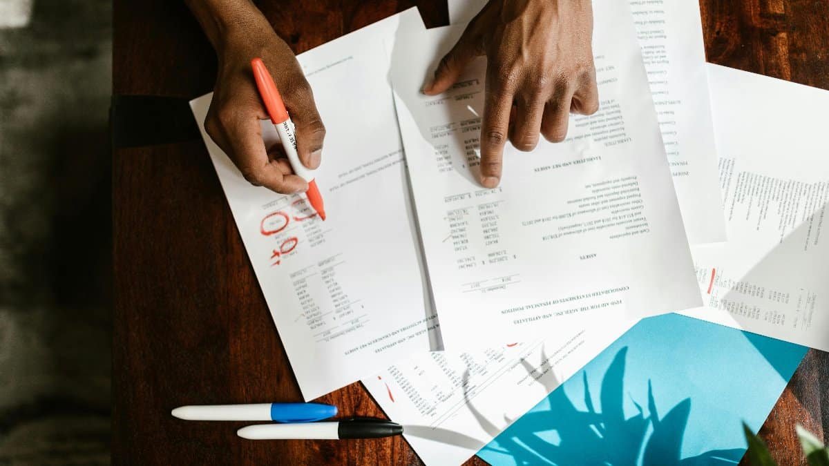 Overhead view of hands highlighting financial documents on a desk. via Pexels