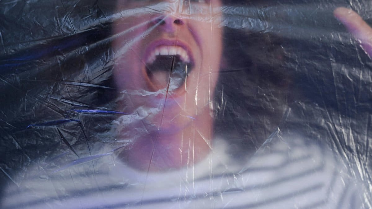 A man in a striped shirt shouting behind a transparent plastic film, creating a dramatic effect. via Pexels