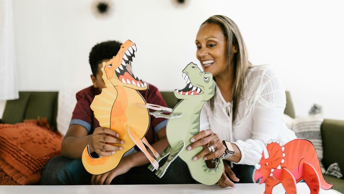 Mother and son share quality time indoors playing with dinosaur crafts, smiling and bonding. via Pexels