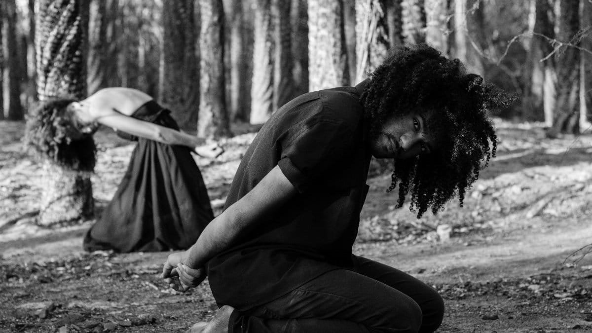 Black and white side view African American couple with hands folded behind back sitting on knees in forest via Pexels