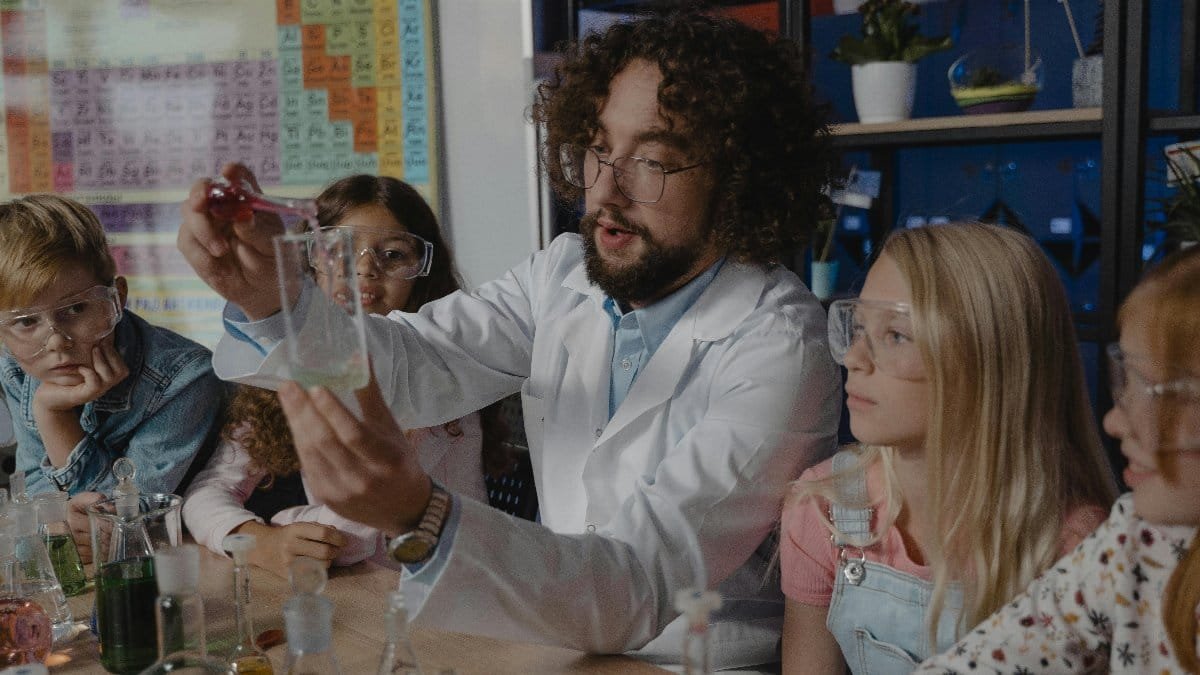 Students engaged in a hands-on chemistry experiment with a teacher in a classroom setting. via Pexels