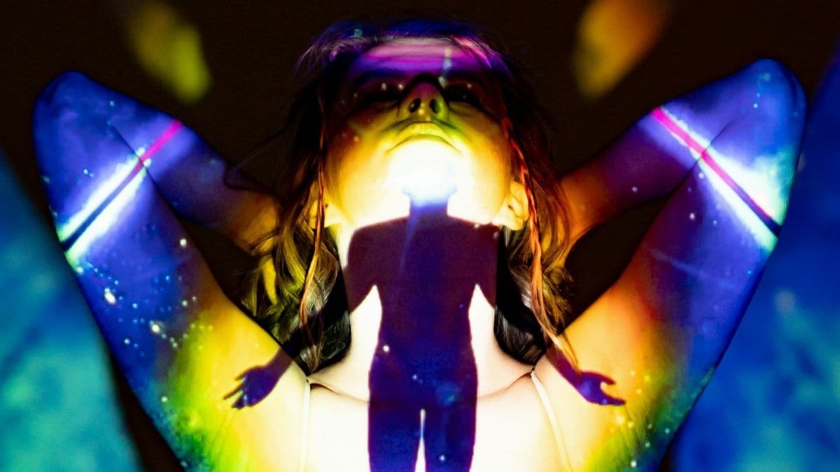 A silhouette emerges through colorful projections, evoking spirituality and energy. via Pexels