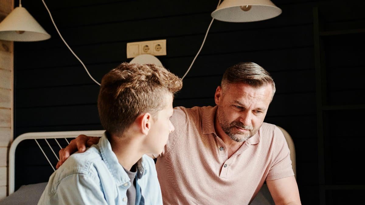 Father and son having a meaningful talk in a cozy bedroom setting. via Pexels