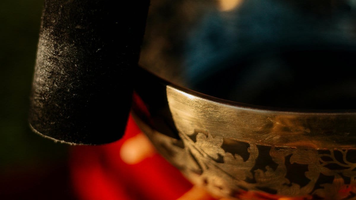 Close-up of a Tibetan singing bowl used for meditation and relaxation, with a hand gently holding the striker. via Pexels