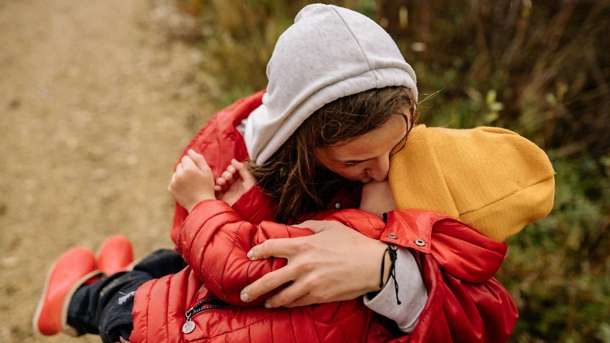 Two children in colorful attire share a warm embrace on a nature trail. via Pexels