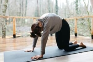 Woman in gray long sleeve shirt and black leggings doing yoga on black yoga mat