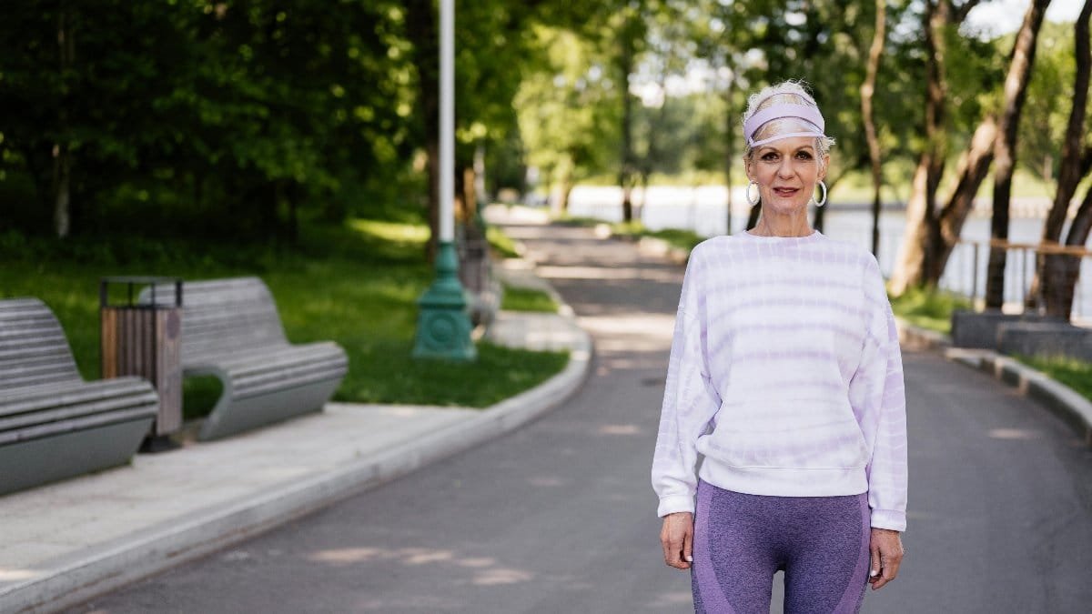 Senior woman in activewear enjoying a walk in a sunny park setting. via Pexels