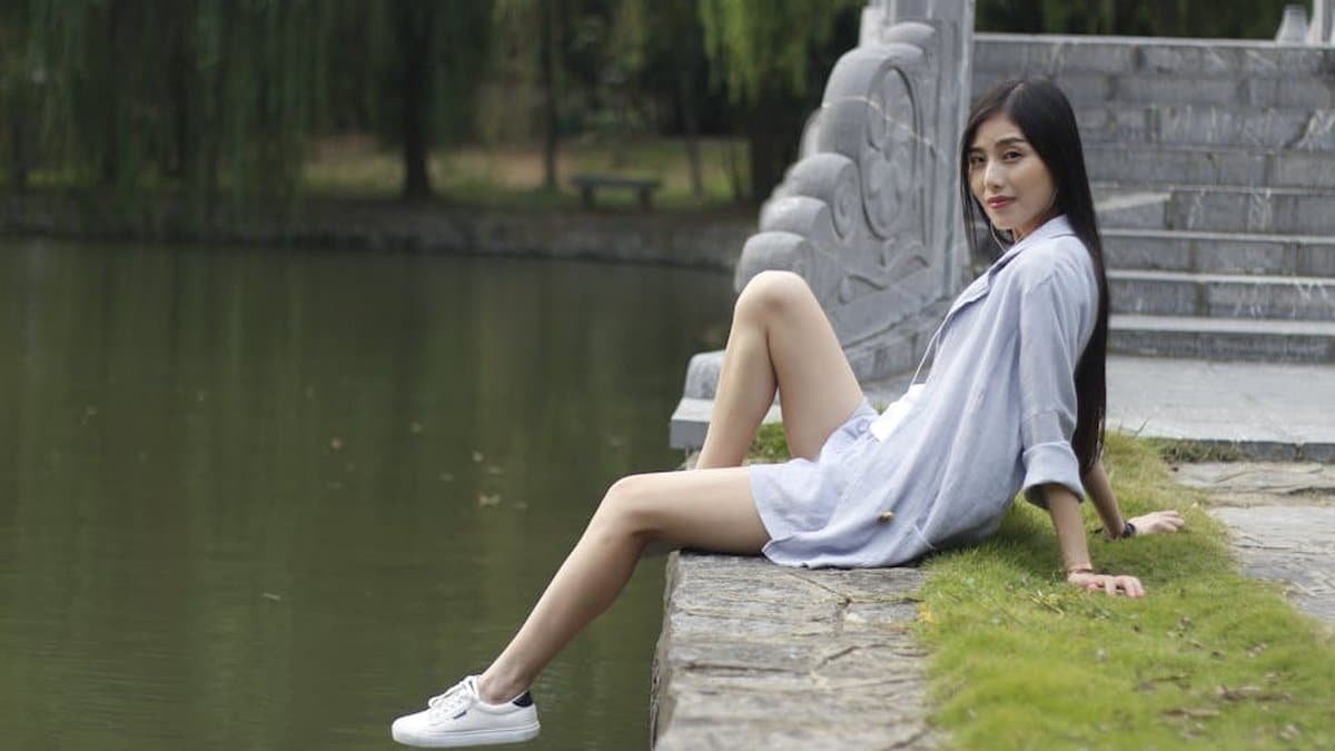 Asian woman enjoying leisure time by a serene lake in summer. via Pexels