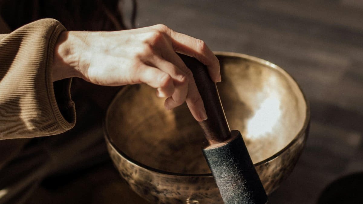 Hand holding a mallet over a Tibetan singing bowl for meditation practice. via Pexels